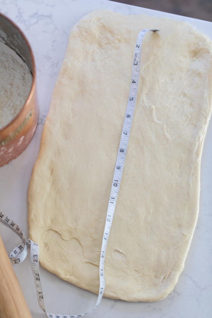 sourdough dough rolled out onto a white quartz countertop with a measuring tape over top of the dough