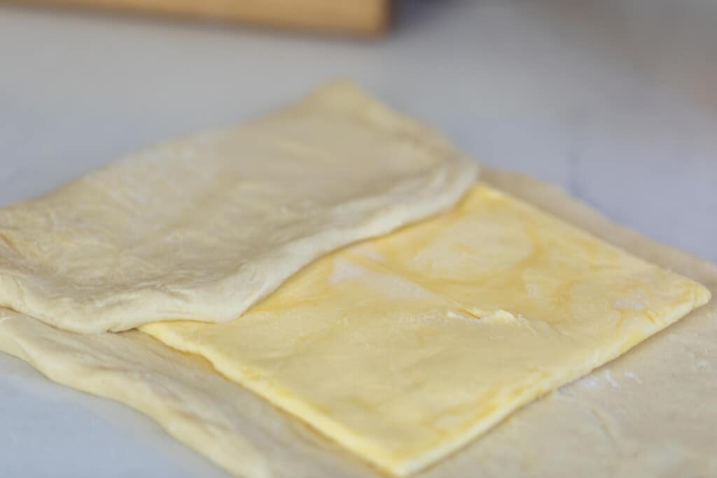 a rectangle of butter on pastry dough and a third of the dough is folded over on top of the butter
