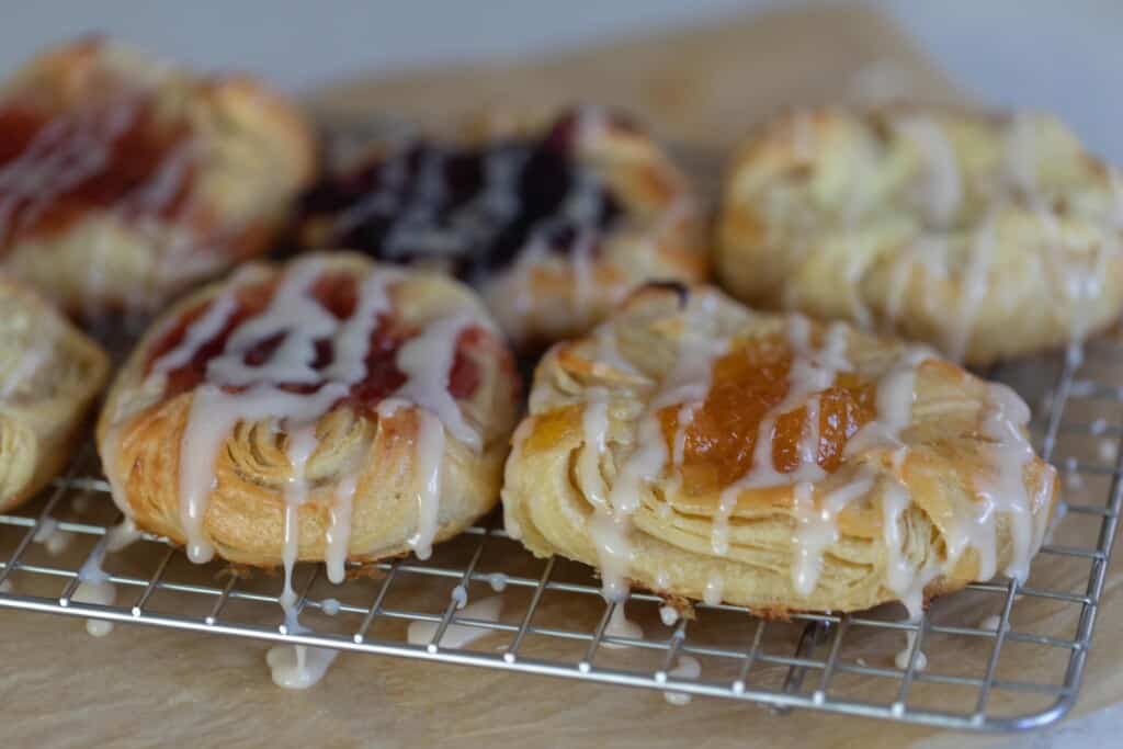 six sourdough pastries with fruit and cream cheese filling and drizzled with a sweet glaze on a wire rack over parchment paper