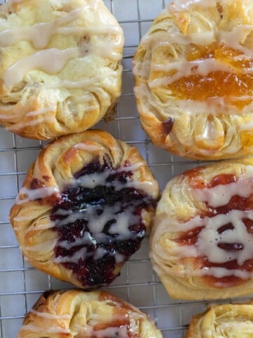 overhead photo of Danish sourdough pastries topped with cream cheese filling and jam and drizzled with a glaze on a wire rack