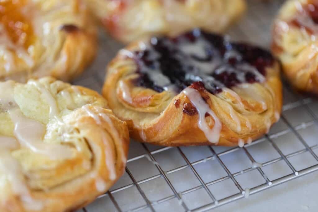 Sourdough Danish pastry with jam and cream cheese filling drizzled with a glaze on a wire rack