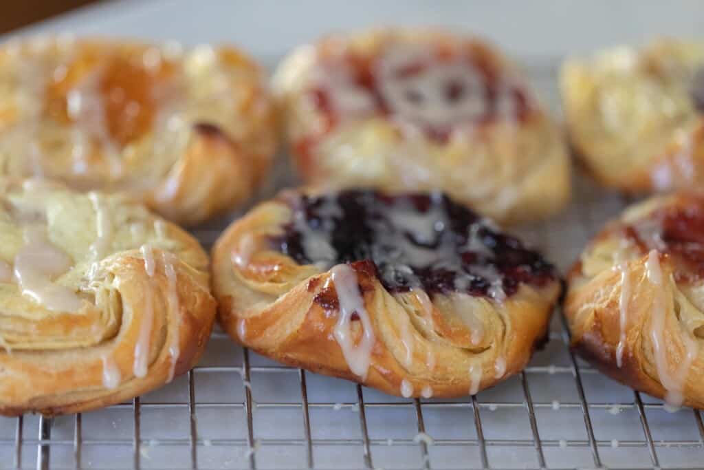 six Danish sourdough pastries with filling and drizzled with glaze on a wire rack