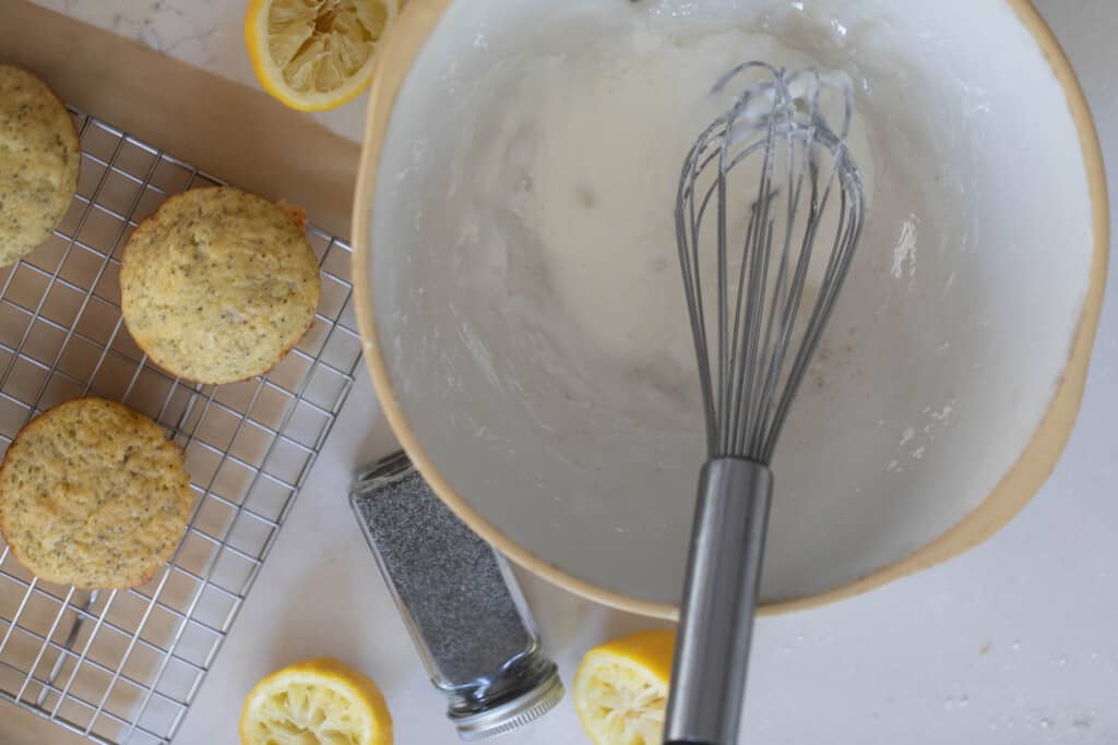 lemon drizzle in a stone bowl with a whisk and muffins to the right