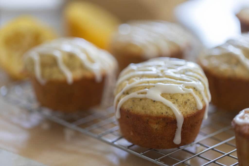 four lemon poppy seed sourdough muffins with a lemon glaze on top of a wire rack with lemon in the backgrounds 