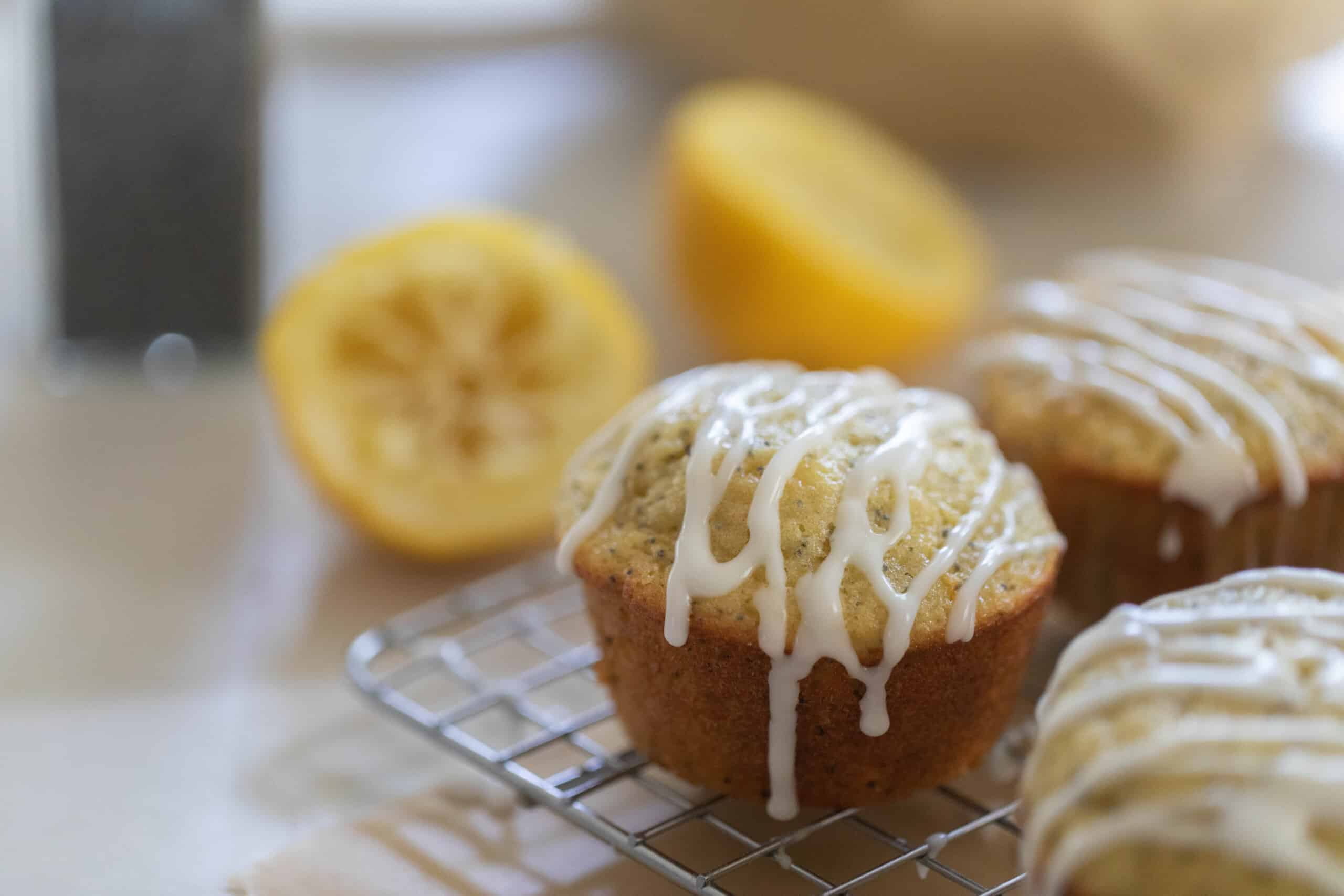 three sourdough lemon poppy seed muffins on a wire rack with two lemon halves in the background