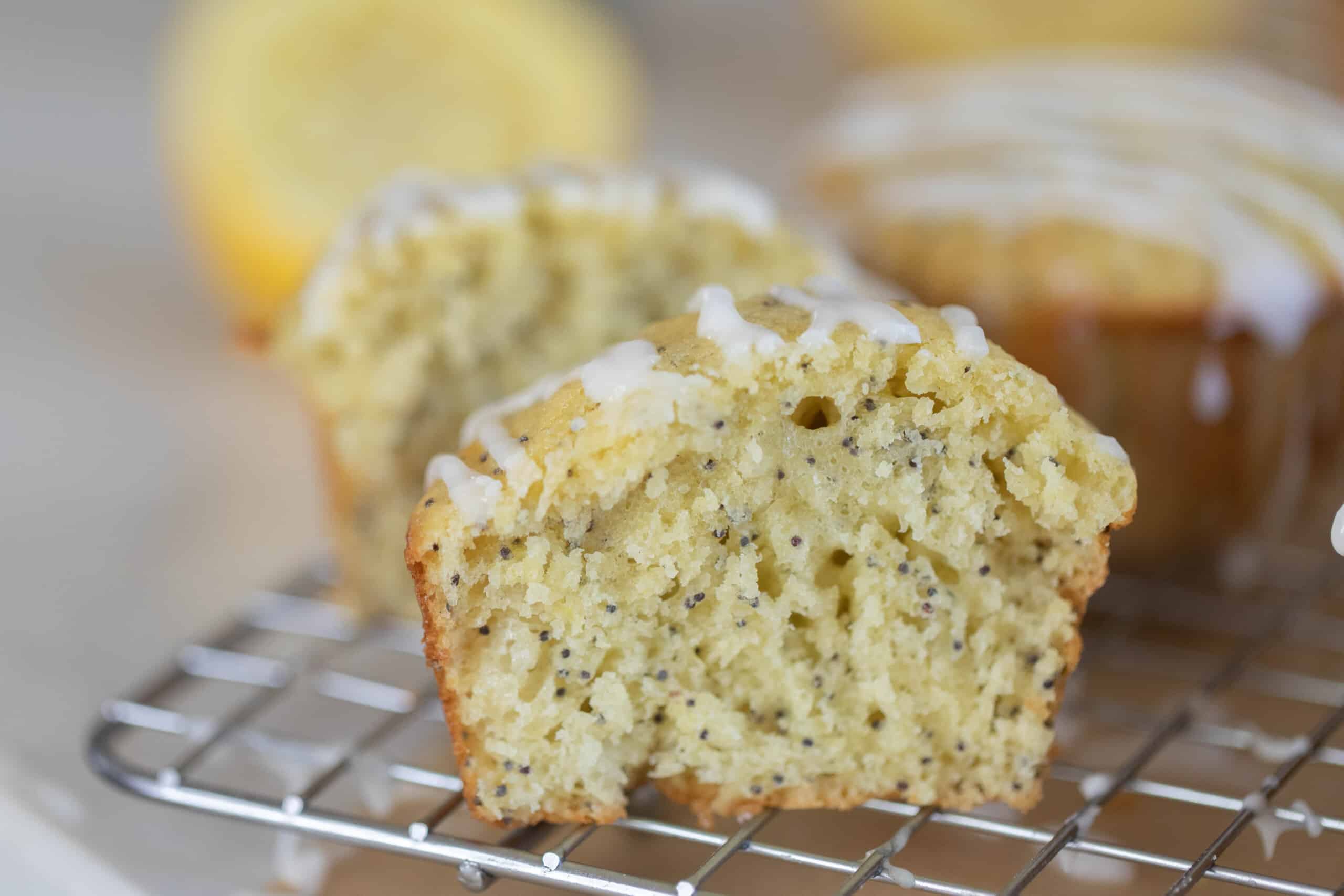 sourdough lemon poppyseed muffin sliced in half of a wire rack. Another muffin and a half of a lemon are in the background