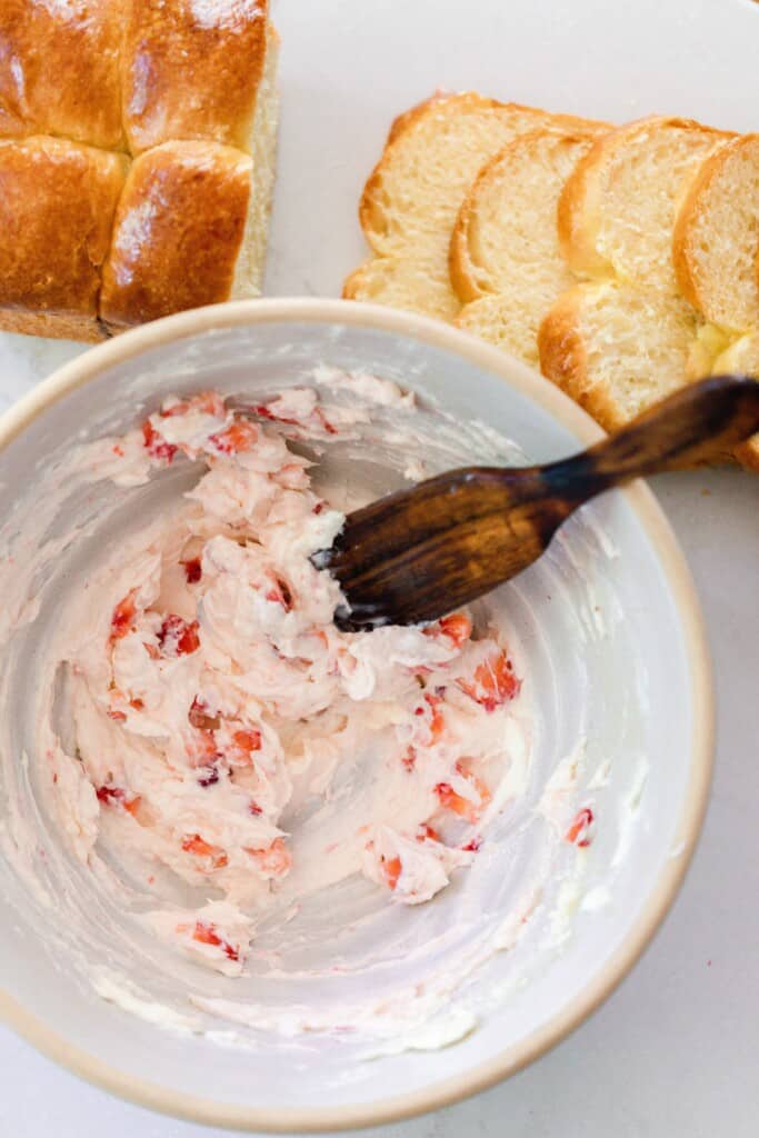 chopped strawberries mixed into sweetened cream cheese in a stoneware bowl with slices of brioche in the background