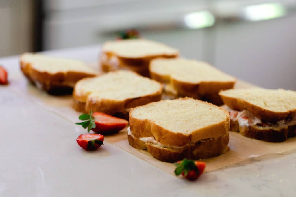 unbaked strawberry stuffed French toast on parchment paper with strawberries scattered around on a white countertop