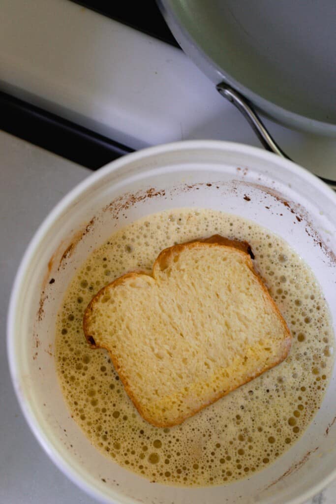 unbaked stuffed French toast soaking in a custard mixture in a white bowl