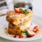 Strawberry stuffed French toast sliced in half and stacked on top of each other topped with powdered sugar and fresh strawberries on a white plate