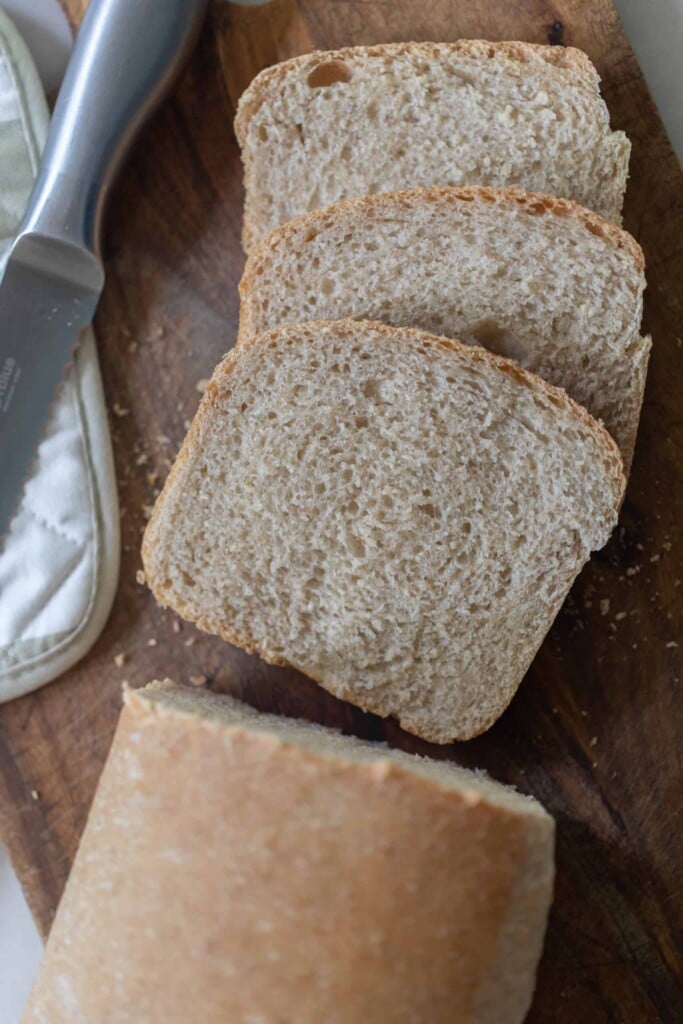 overhead photo of a loaf of whole wheat sourdough sandwich bread with three slices sliced off the loaf and laying on a wooden cutting board