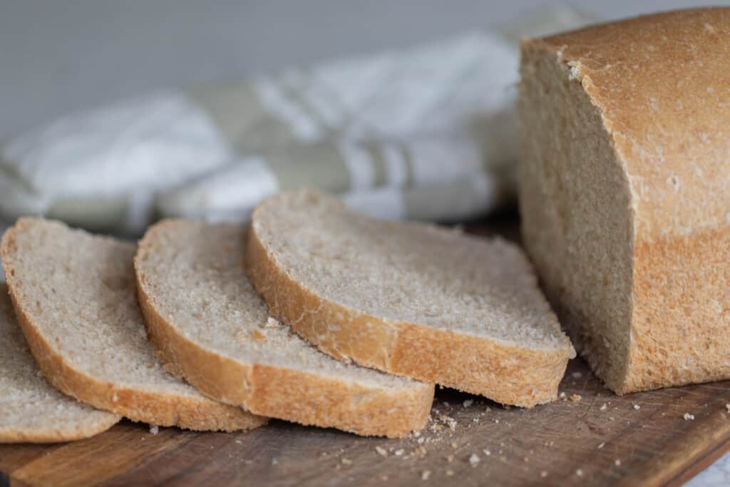 loaf of sourdough sandwich bread with four slices cut and laying on a wooden cutting board