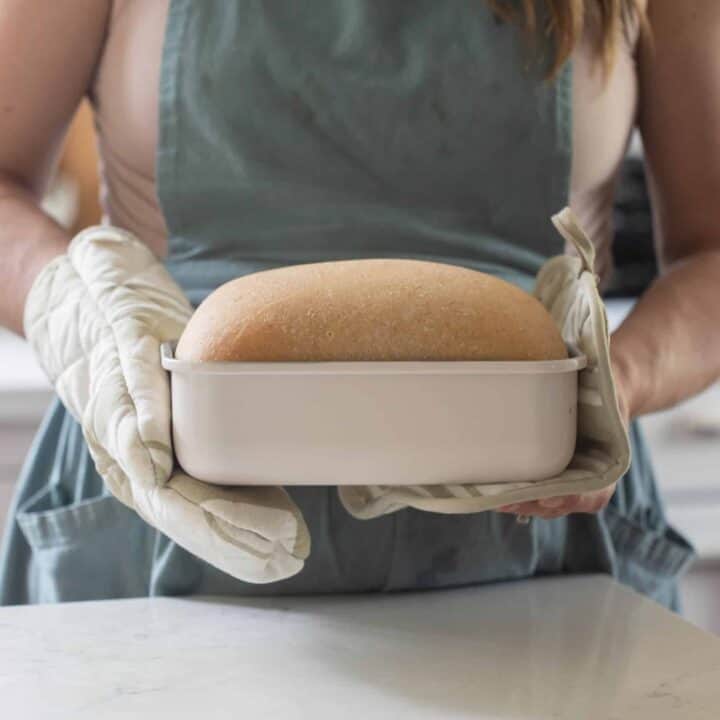 woman wearing a blue apron holding a white loaf pan of bread
