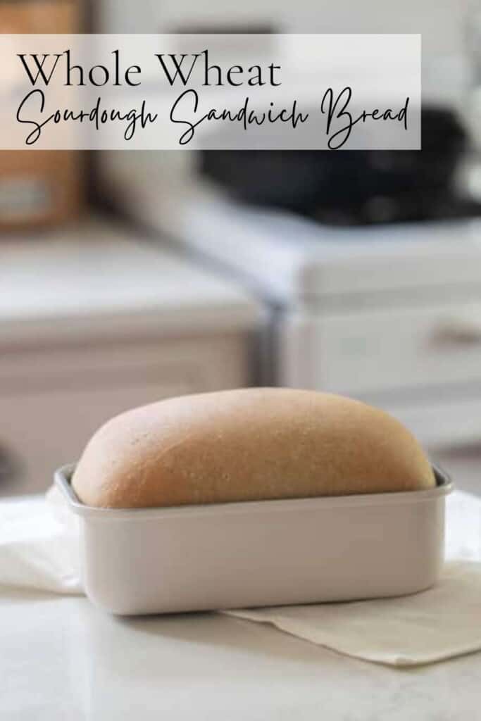 loaf of whole wheat sourdough sandwich bread in a white loaf pan on a white kitchen island with a antique stove in the background