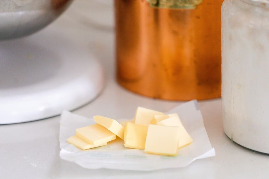 slices of butter on a butter wrapper on a white countertop with canisters surround the butter