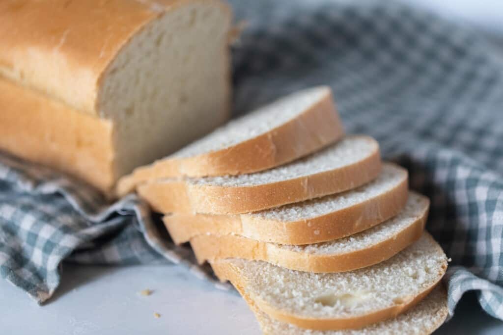 loaf of buttermilk sourdough bread with slices falling from the loaf on a white and blue checked towel