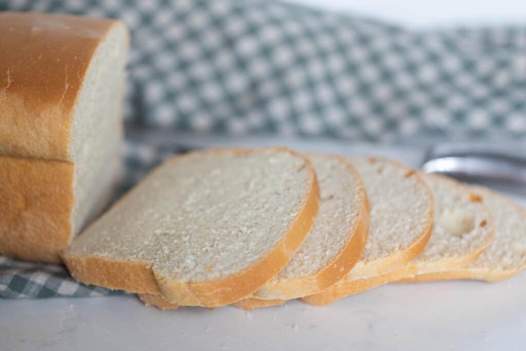 slices of sourdough buttermilk bread off of a loaf of bread with a blue and white check towel in the background