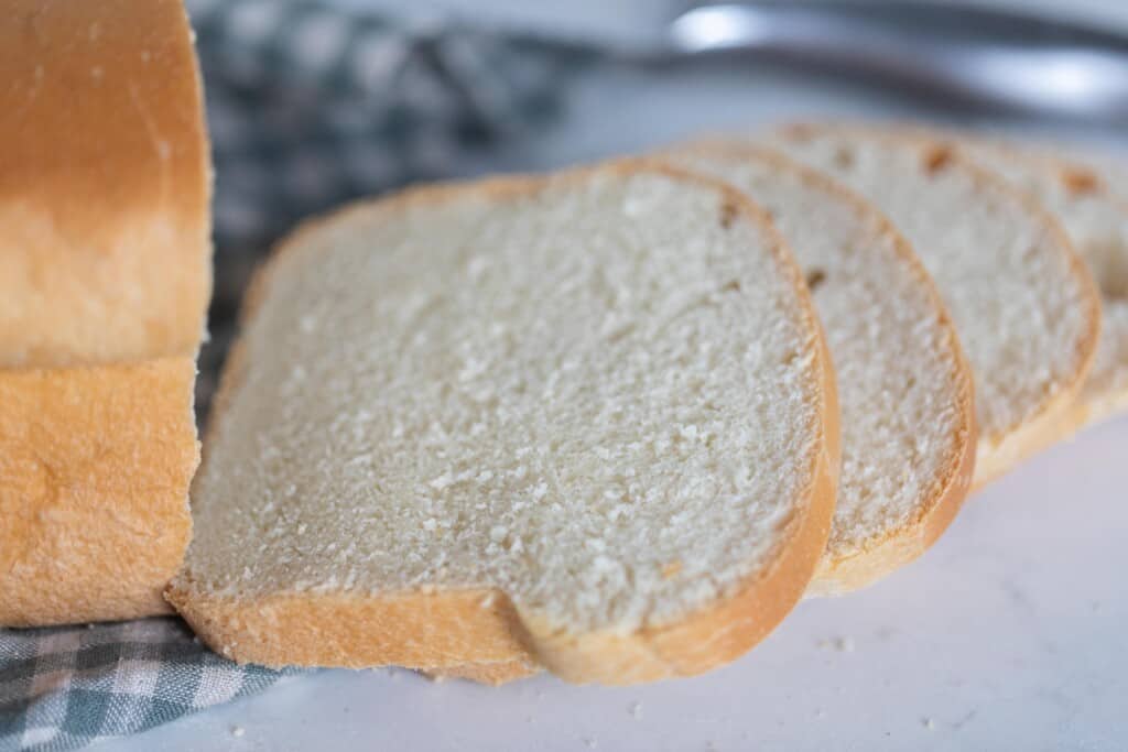 three slices of buttermilk sourdough bread slices on a white countertop with a blue and white checked towel to the left