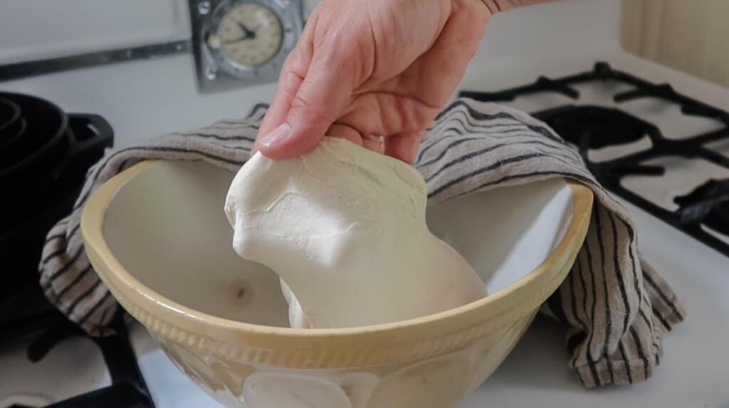 hands grabbing dough out of the bowl to show the dough passing the windowpane test