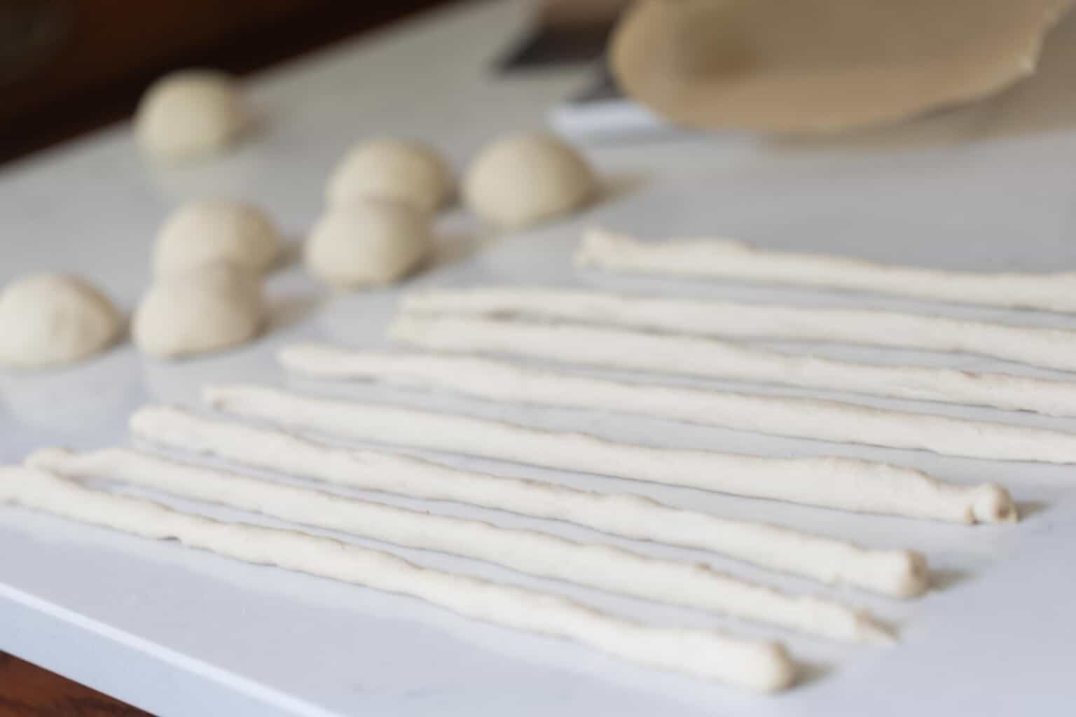 discard pretzel dough rolled into ropes on a white countertop with more dough balls to the left