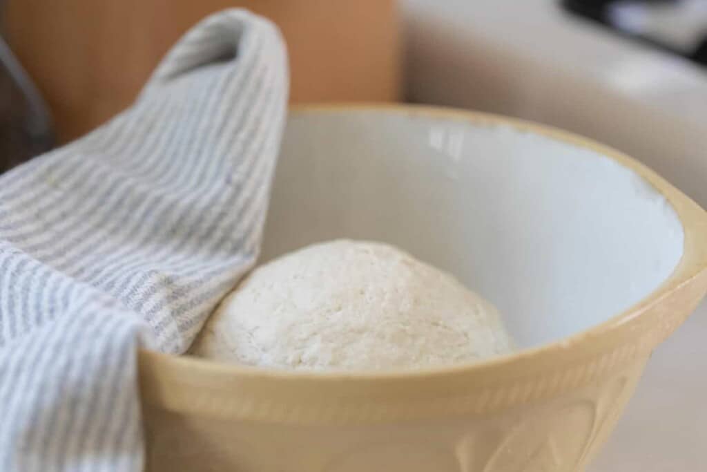 dough in a ironstone mixing bowl with a tea towel over a corner of the bowl