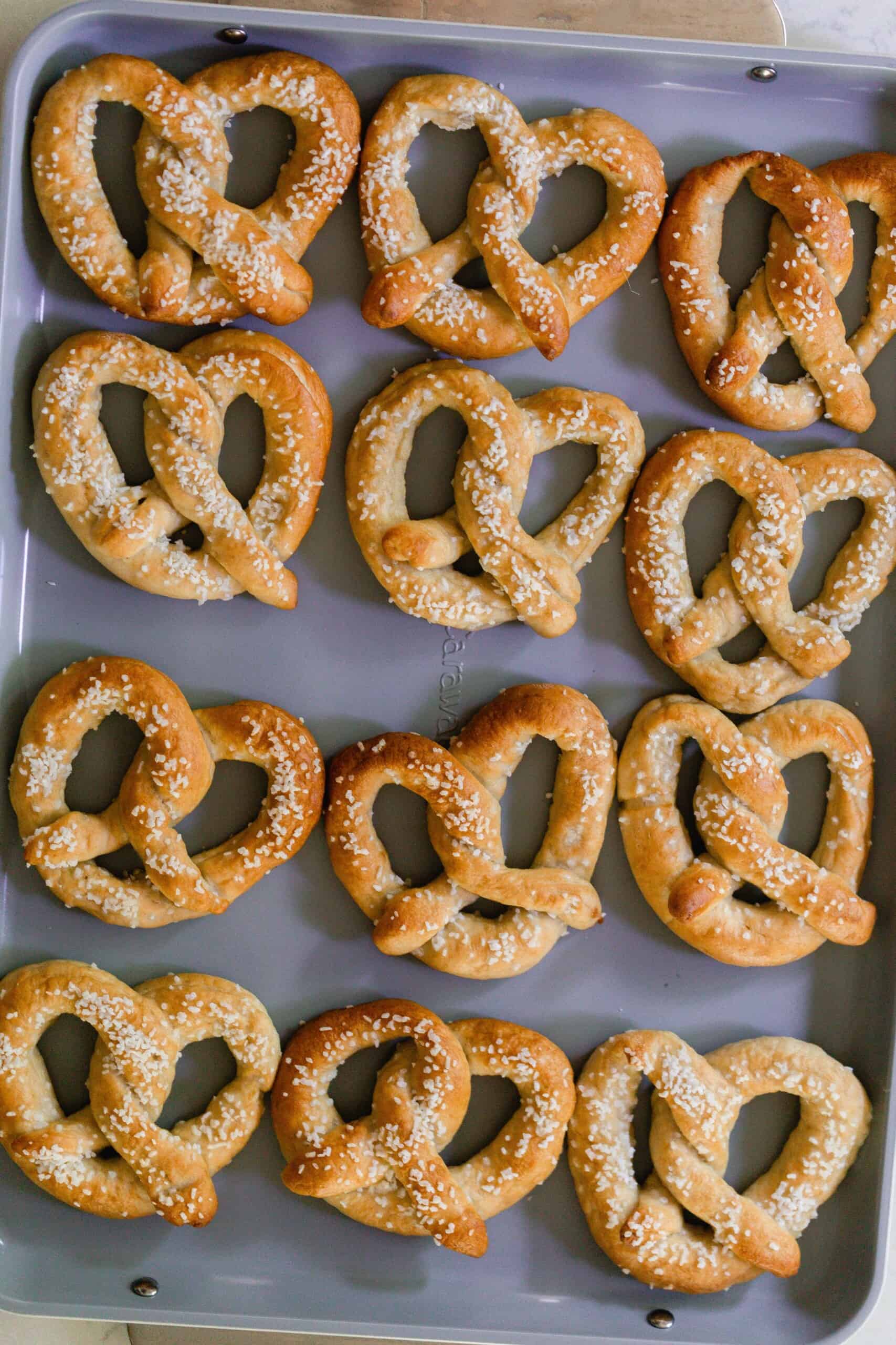 Baking sheet with freshly baking homemade sourdough pretzels topped with coarse salt