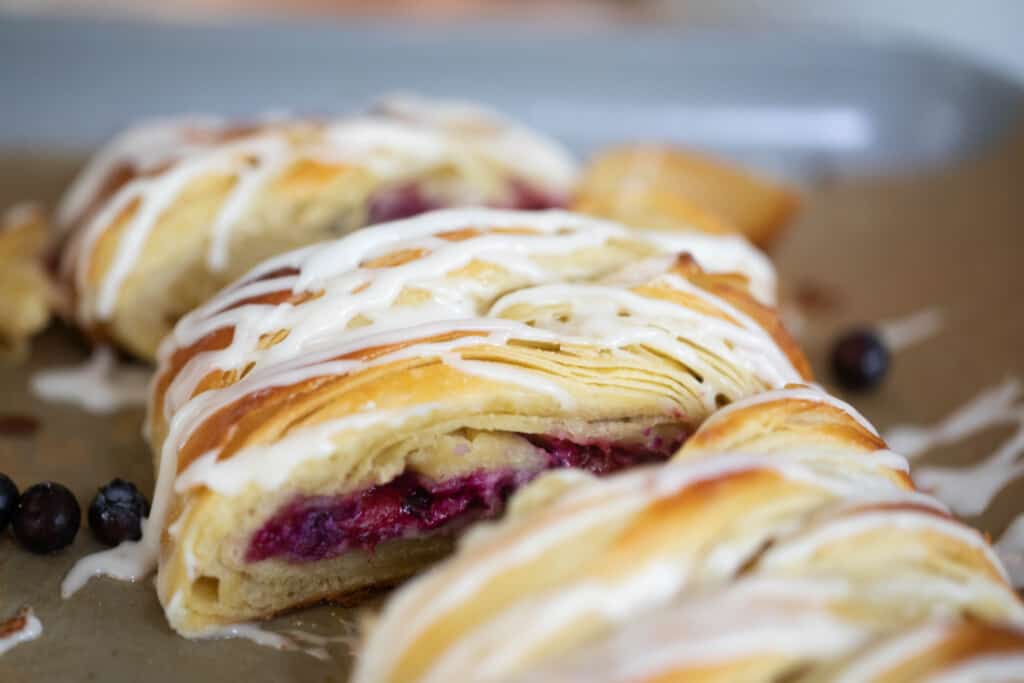 sourdough blueberry cream cheese pastry braid drizzled with icing on parchment paper