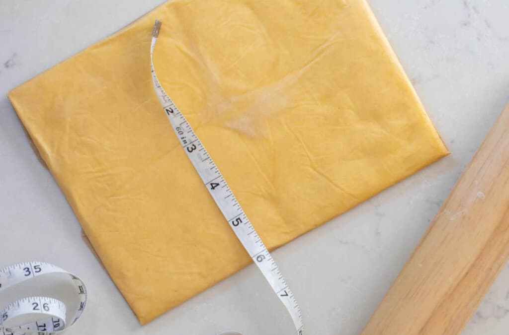 butter rolled out in a rectangle on a white countertop with a rolling pin to the right