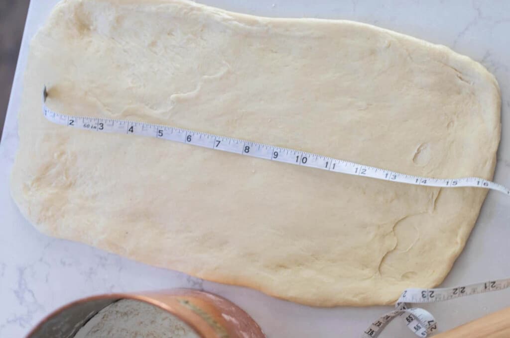 pastry dough rolled out onto a white countertop with a measuring tape on top