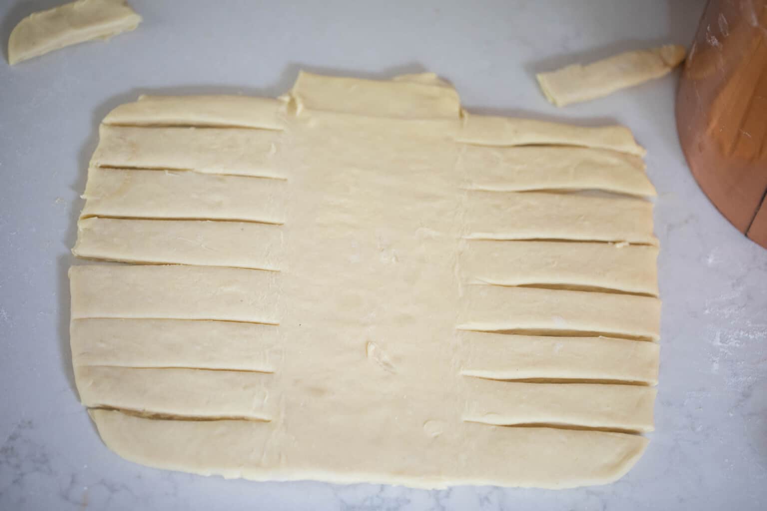 sourdough pastry braid dough rolled out and cut with slits on a white countertop