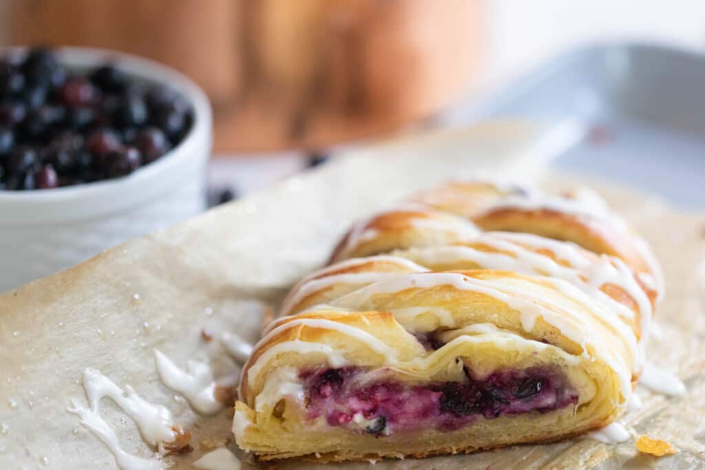sourdough pastry braid with a blueberry cream cheese filling on a parchment lined backing sheet with a bowl of blueberries to the left