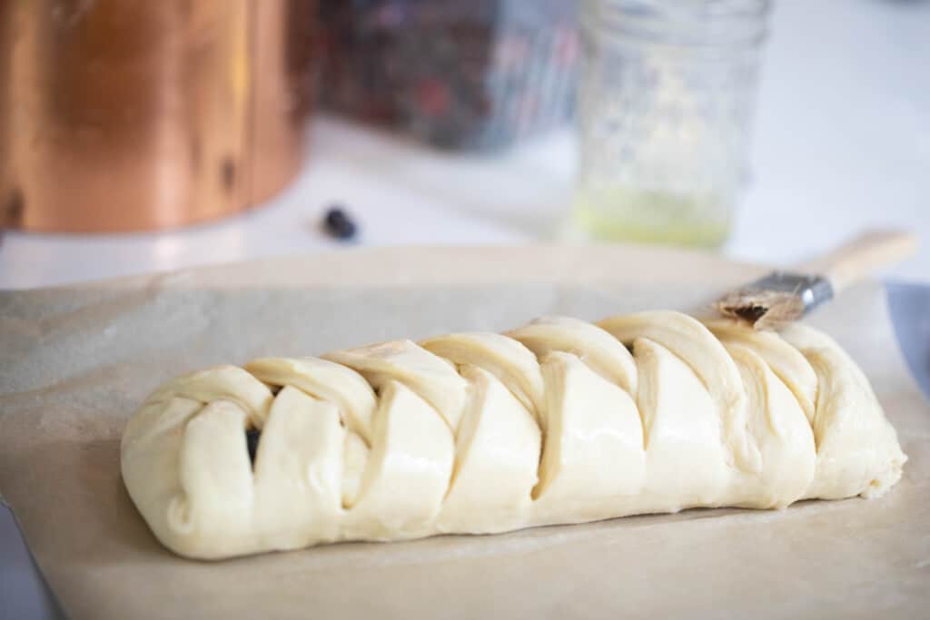 unbaked sourdough pastry braid on parchment paper with a copped canister and glass jars in the background