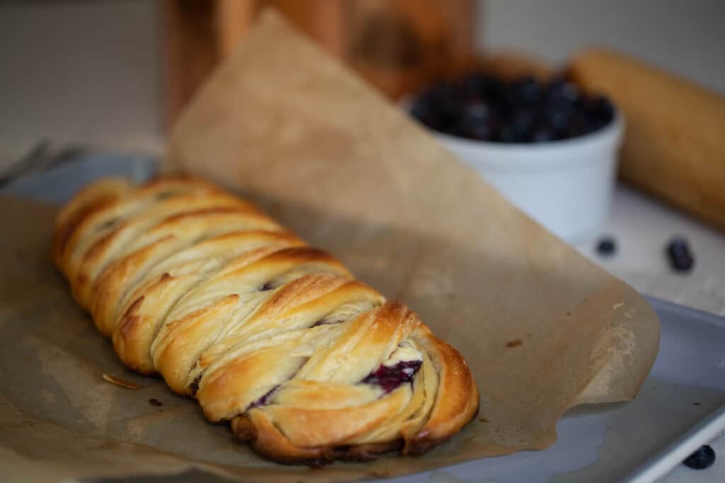 sourdough blueberry pastry braid on parchment paper lined baking sheet with a bowl of blueberries in the background