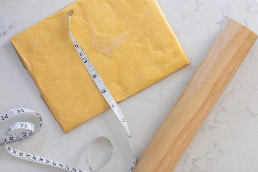 butter rolled out into a rectangle with a measuring tape across the butter and a rolling pin the right 