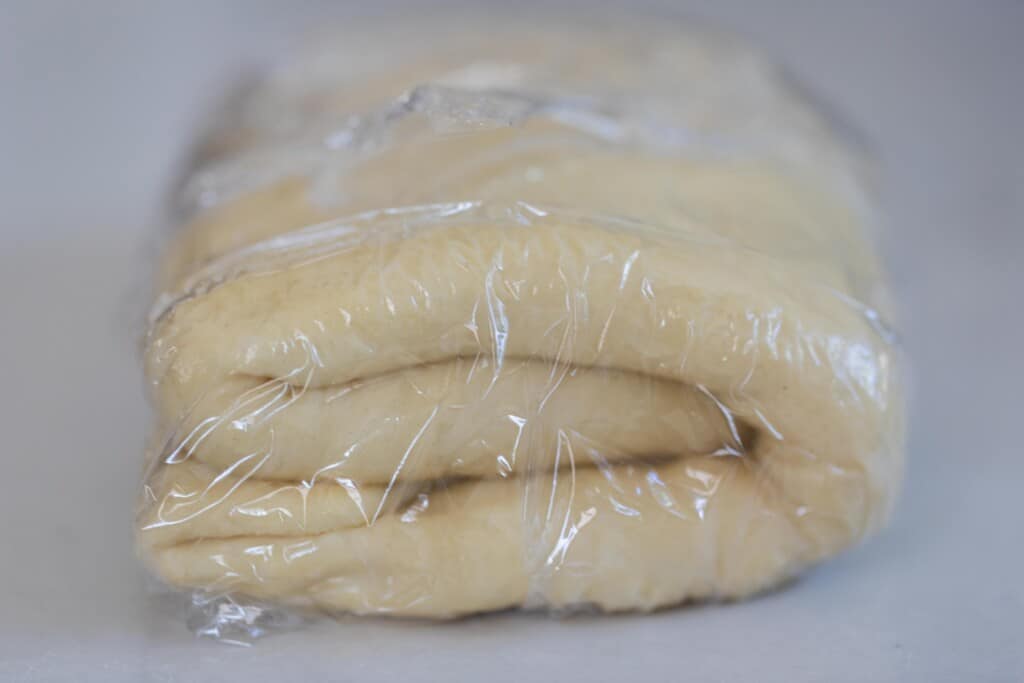 sourdough pastry dough folded into fourths and wrapped in plastic wrap on a white countertop