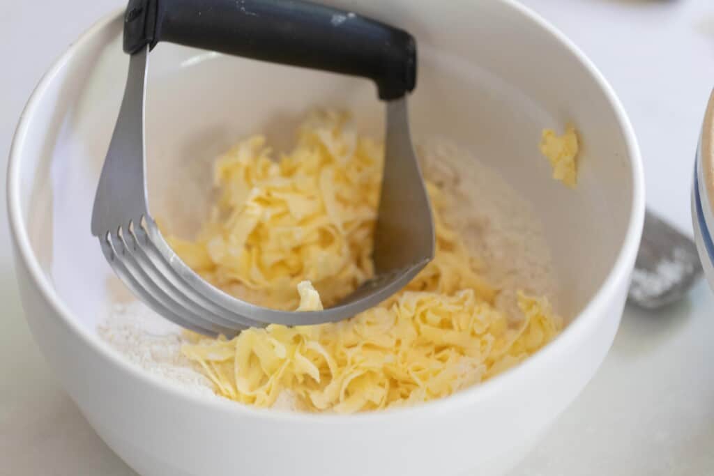 frozen grated butter with flour in a large white bowl with pastry blender