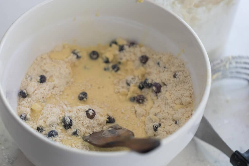 wet ingredients adding to butter flour mixture with blueberries into a large white bowl