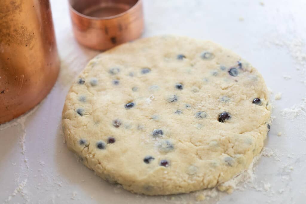 scone dough in a circle shape on a white quartz countertop with copper containers in the background