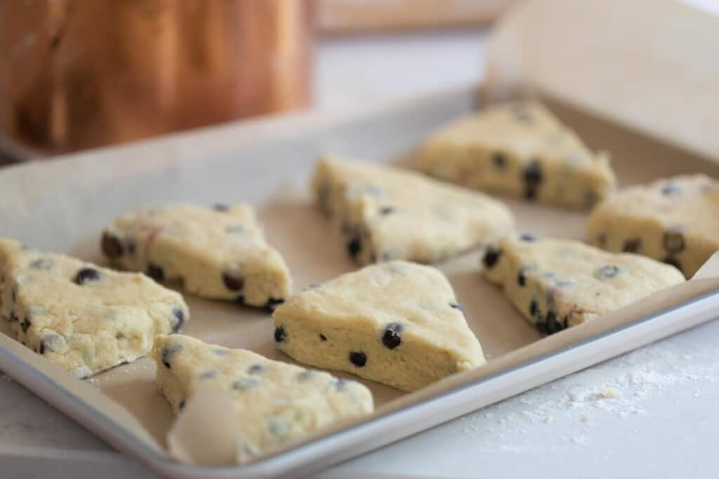 unbaked blueberry sourdough scones on a parchment lined backing sheet on a white quartz counter with a copper container in the background