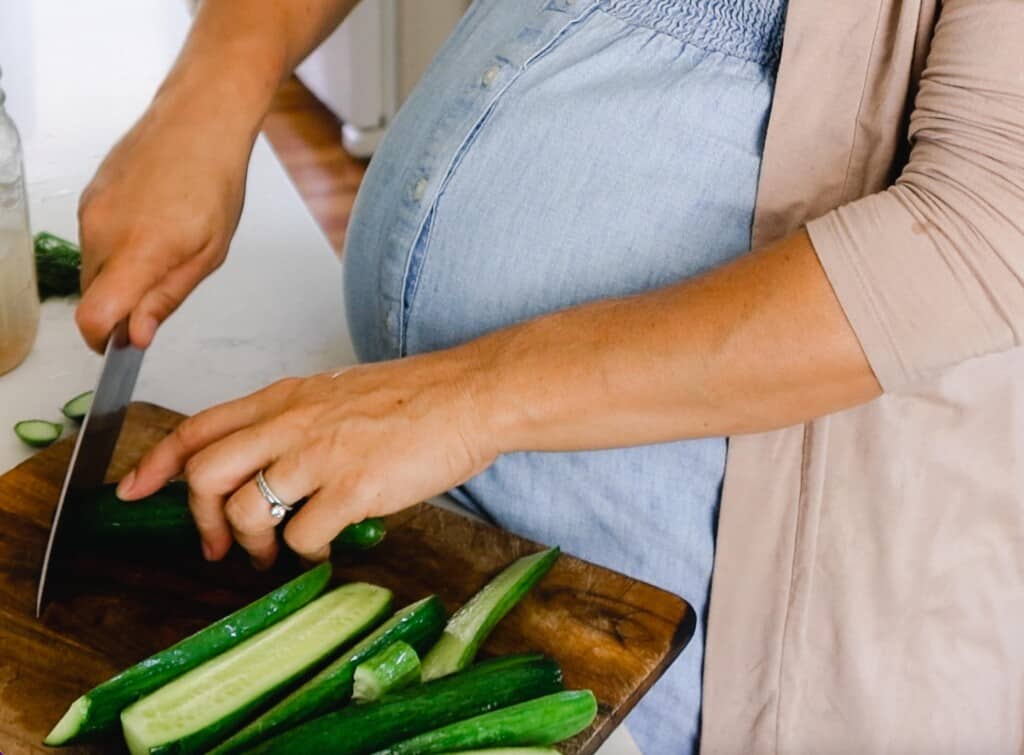 woman wearing a blue dress slicing cucumbers on a wood cutting board