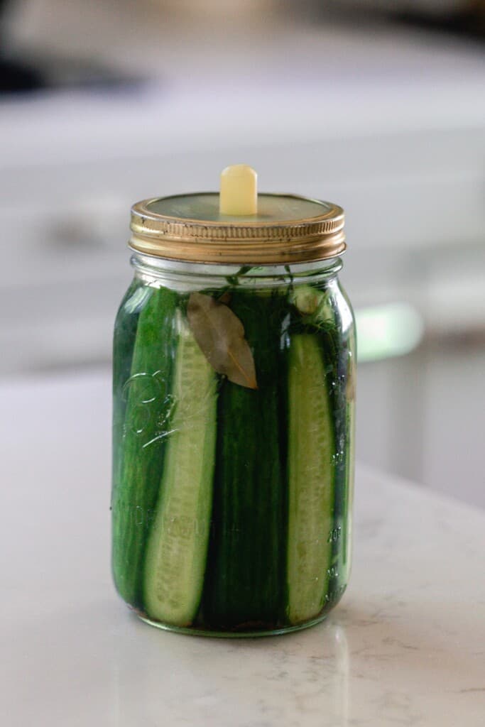 fermented pickles in a mason jar with a silicon fermentation lid. The jar sits on a white countertop with a vintage stove in the background