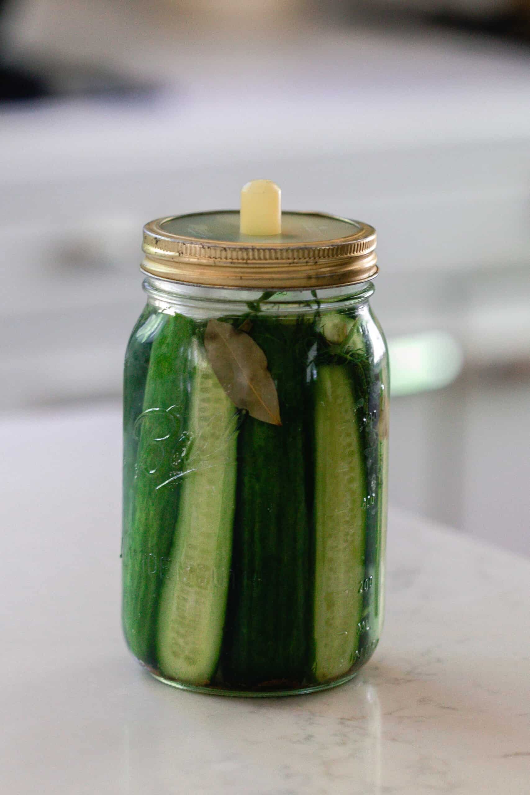 fermented pickles in a mason jar with a silicon fermentation lid. The jar sits on a white countertop with a vintage stove in the background