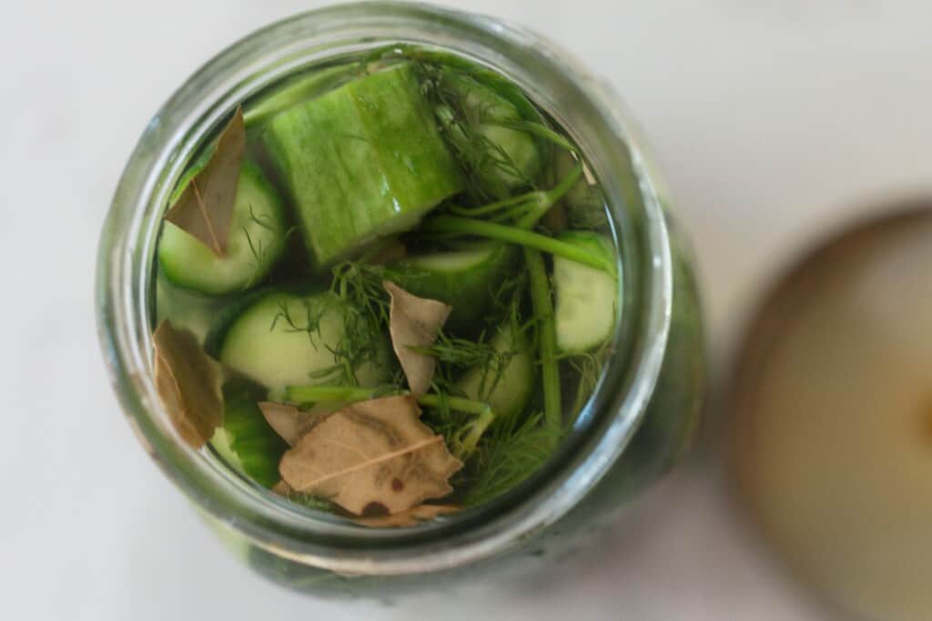 overhead photo of fermented pickles in a mason jar. The jar sits on the white countertop 