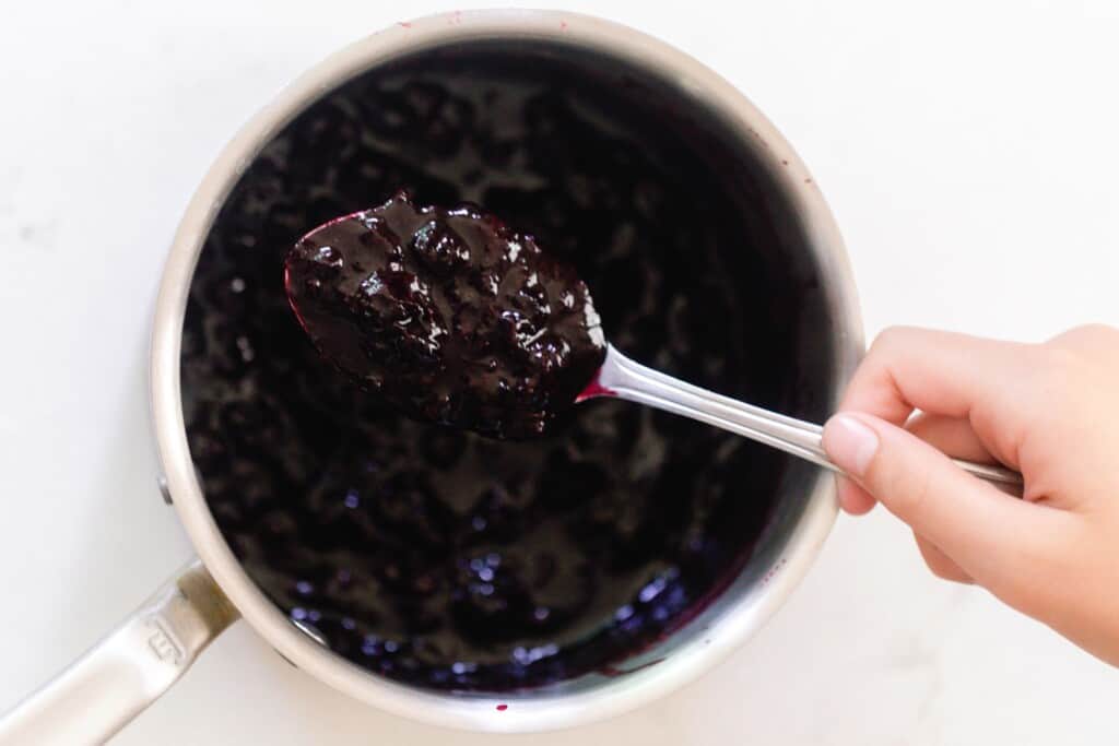 cooked blueberries in a saucepan with a spoonful out