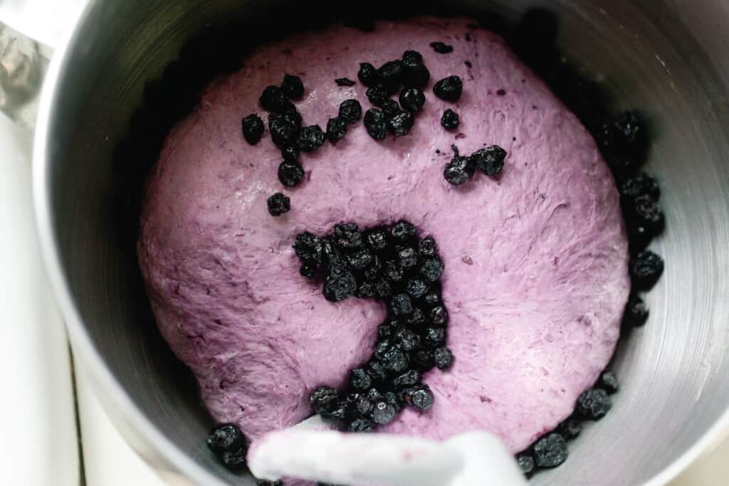 dried blueberries in purple dough in a stand mixer bowl