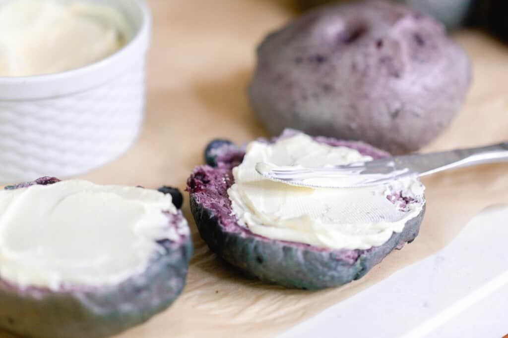 knife spreading cream cheese on blueberry sourdough bagels