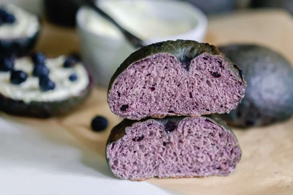 a blueberry sourdough bagel cut in half and stacked on top of each other on parchment with more bagels in the background