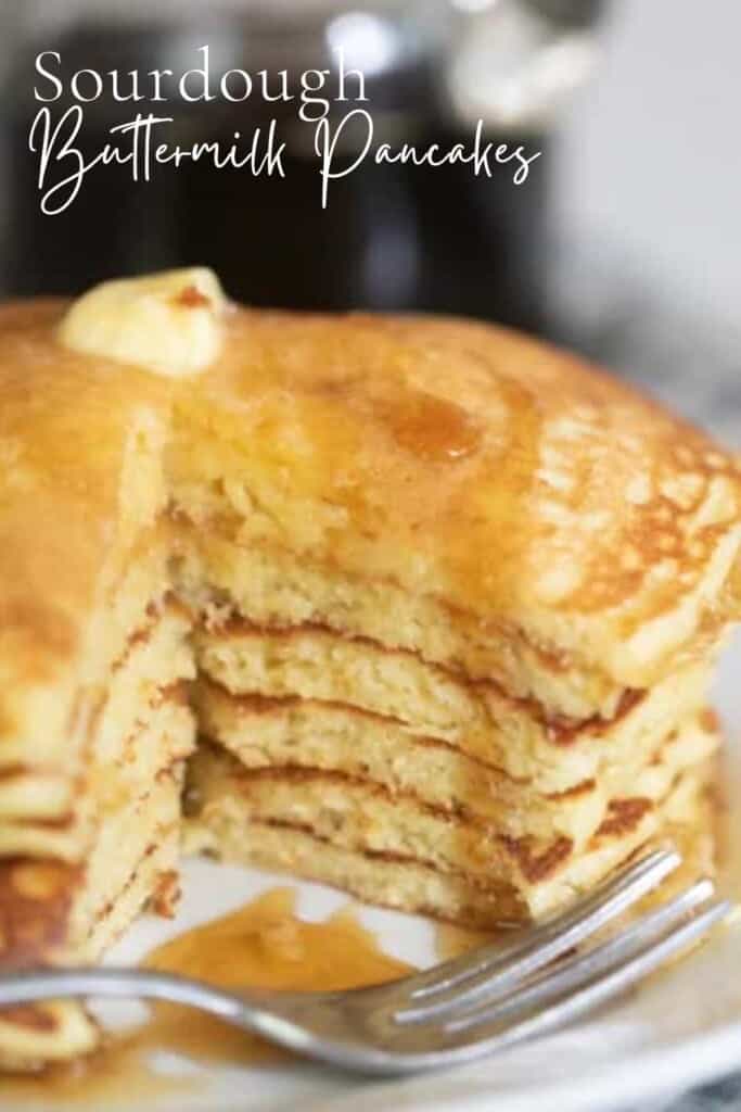 close up of sourdough buttermilk pancakes stacked on a white plate with a sliced taken out of the stack