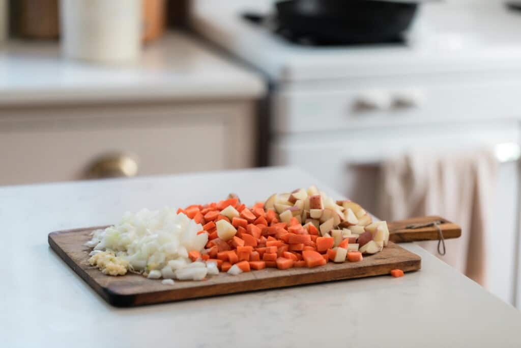 chopped onions, garlic, carrots, and potatoes in a wooden cutting board