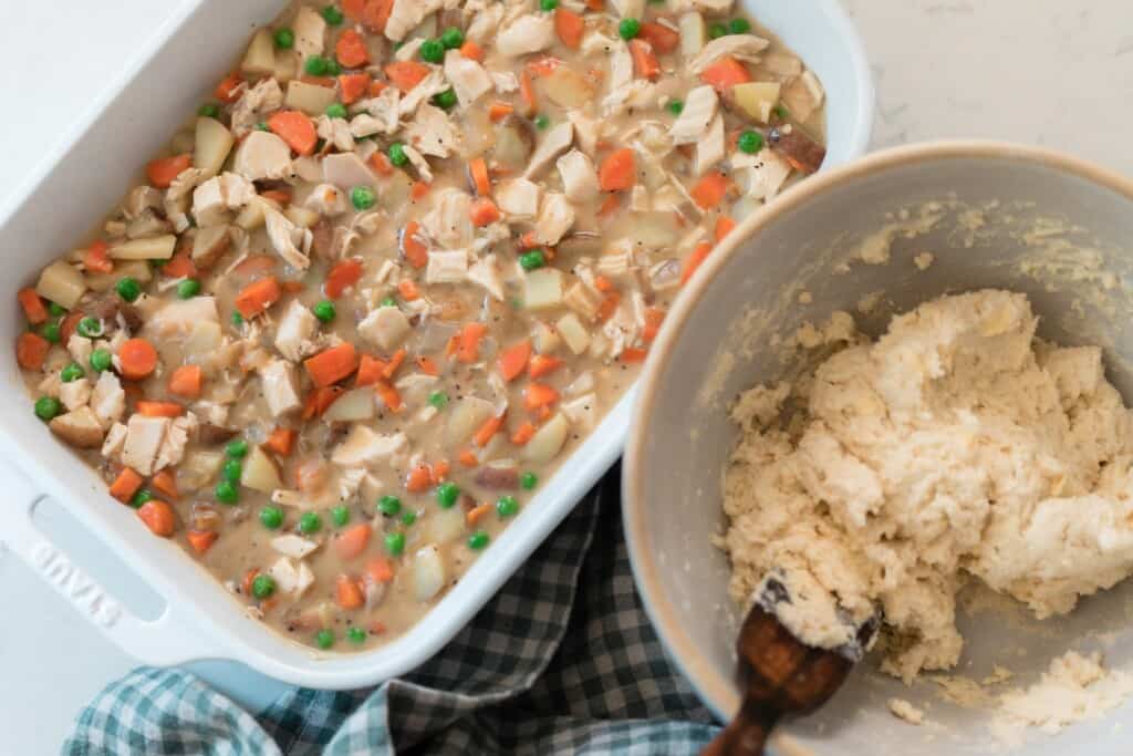 chicken pot pie filling in a white baking dish with a bowl of biscuit dough to the right